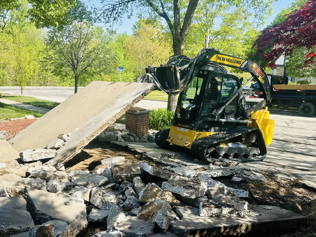 Skid steer lifting a broken slab during removal of an old concrete driveway