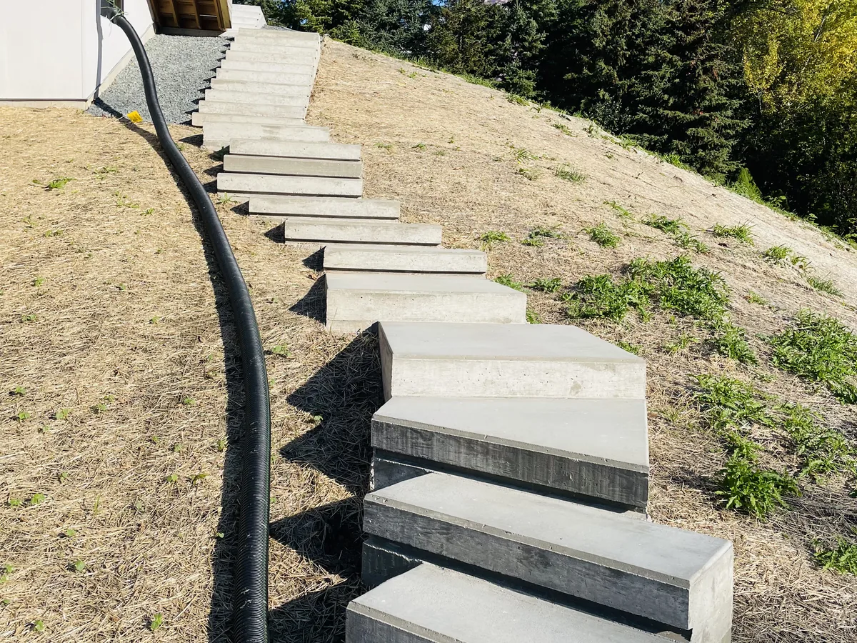 Finished concrete steps descending a grassy hillside with a black metal handrail alongside