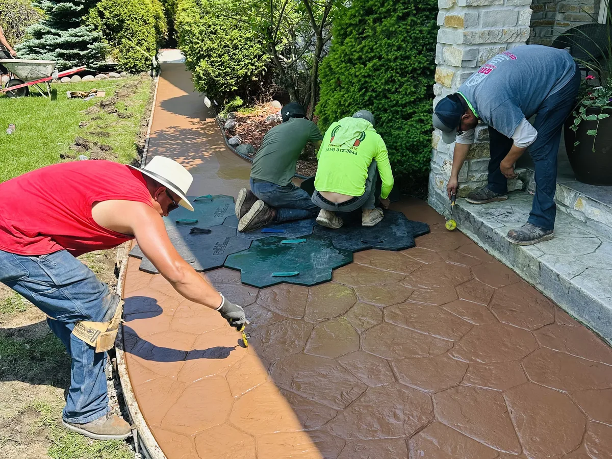 Tan stamped concrete walkway curving alongside a mulched landscaping bed and shrubs